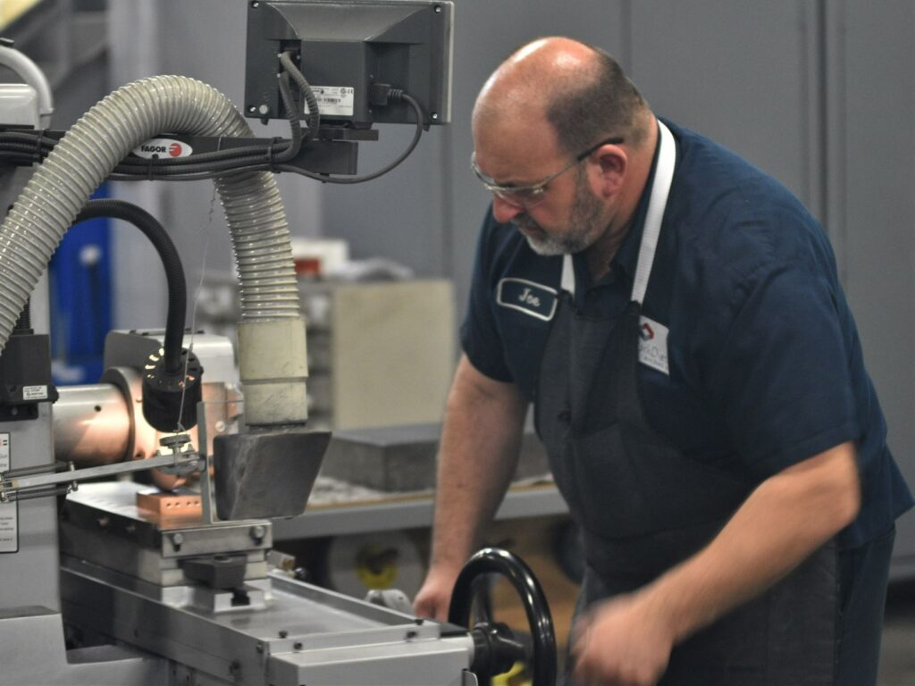 Tool and die maker stands at grinder.